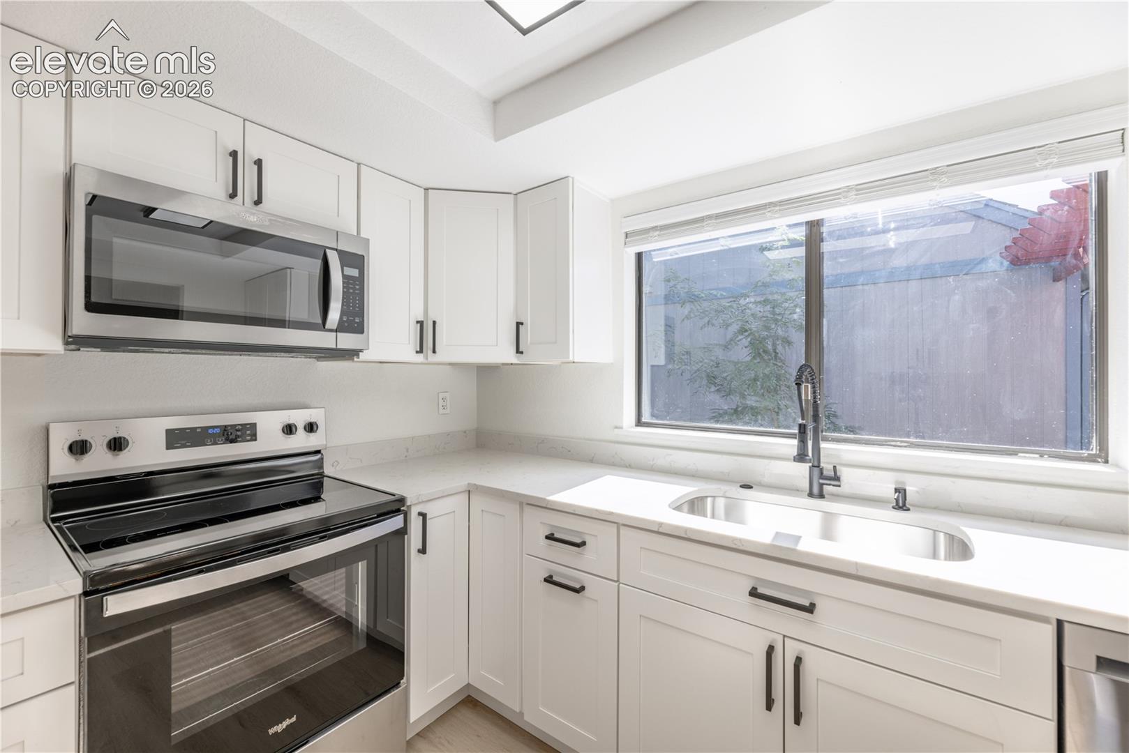 Kitchen featuring white Shaker-style cabinetry, stainless steel appliances, stone-composite countertops, and a gooseneck faucet