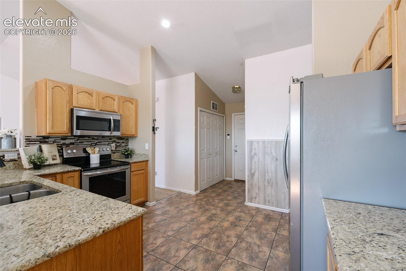 Open and functional kitchen featuring granite countertops, stainless steel appliances, abundant cabinet space, and vaulted ceilings.