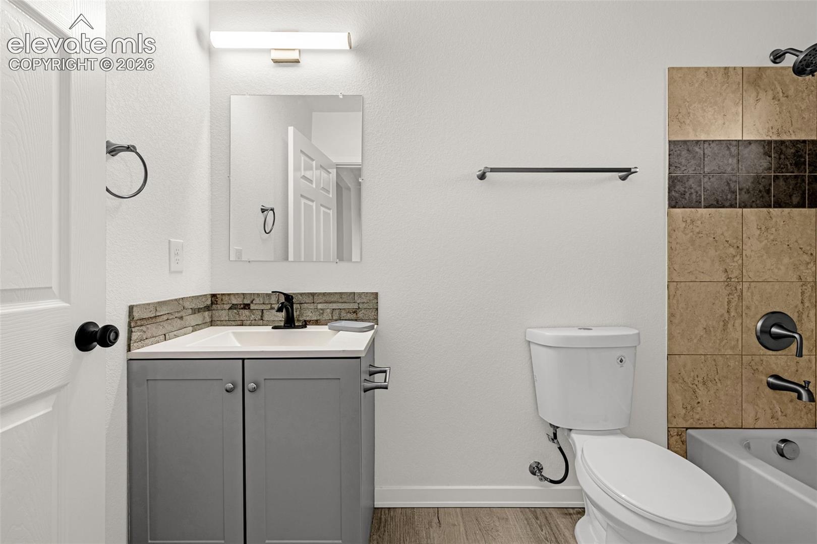 Bathroom featuring a gray vanity with a white countertop, black fixtures, stacked stone backsplash, and wood-finish flooring