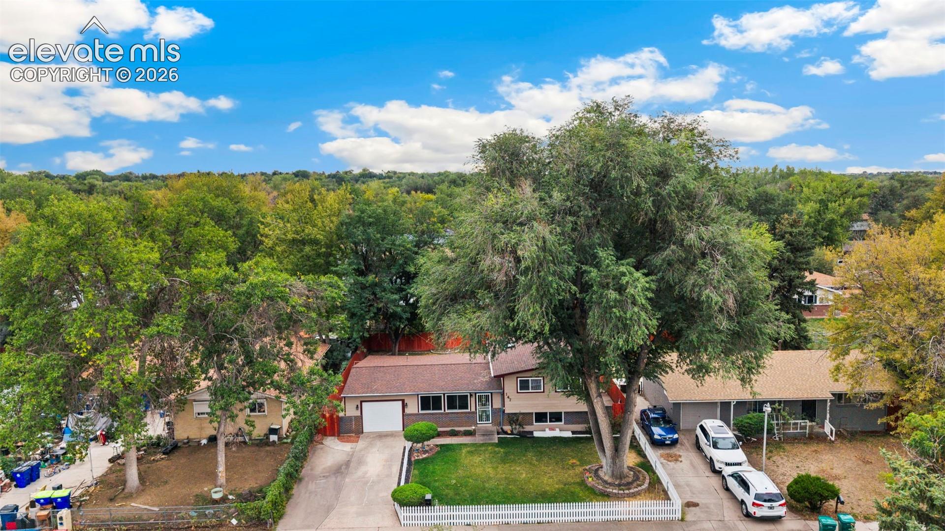 Split-level residence featuring an attached garage, paved driveway, and mature landscaping