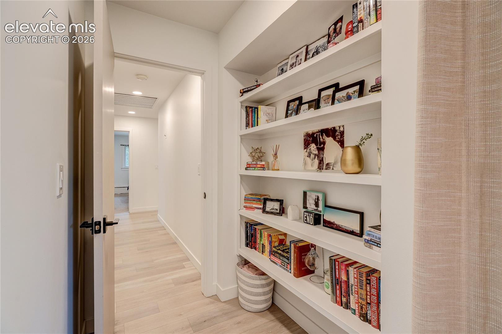 Built-in shelving with multiple display tiers, recessed ceiling lighting, light wood-finish flooring, and crisp white walls