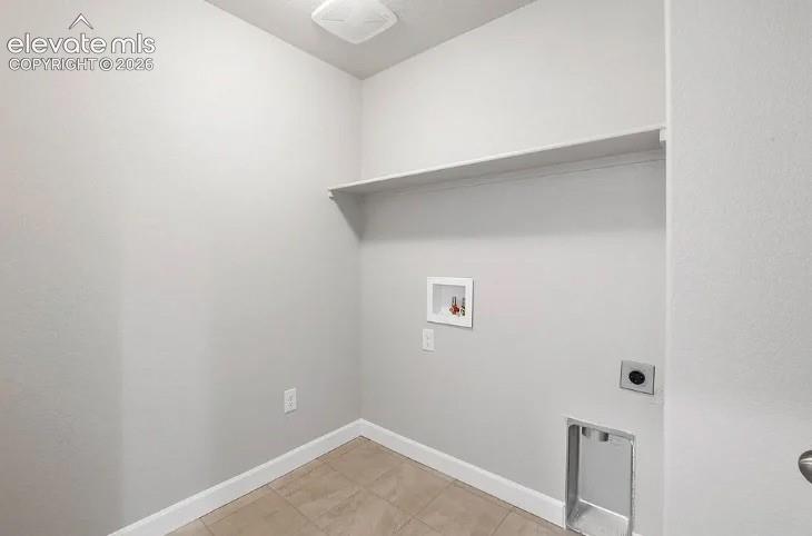 Utility space featuring neutral-toned tile flooring, recessed washer and dryer hookups, and a built-in overhead shelf