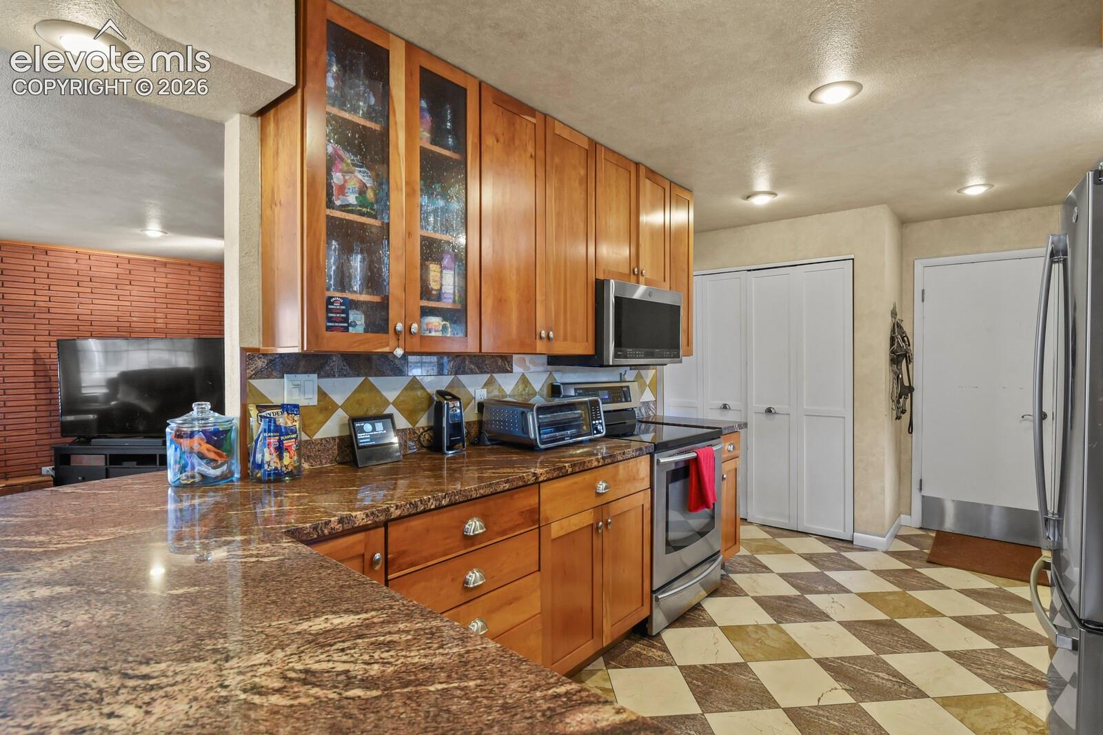 Granite countertops, full-height wood cabinetry with glass-front uppers, stainless steel appliances, and checkerboard floor tiling
