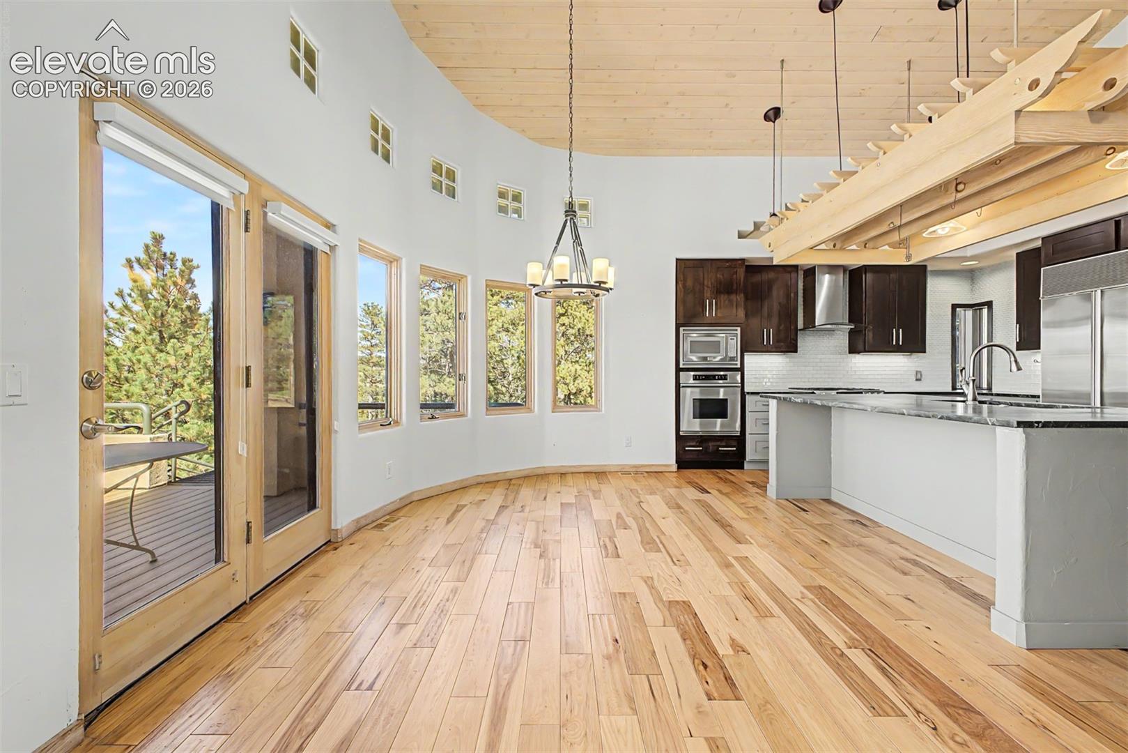 Hardwood flooring, curved wall with multiple windows, glass-paneled patio doors, kitchen island with built-in sink, and stainless steel appliances