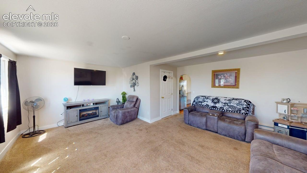 Carpeted living area with light-colored walls and a window featuring dark-colored drapes