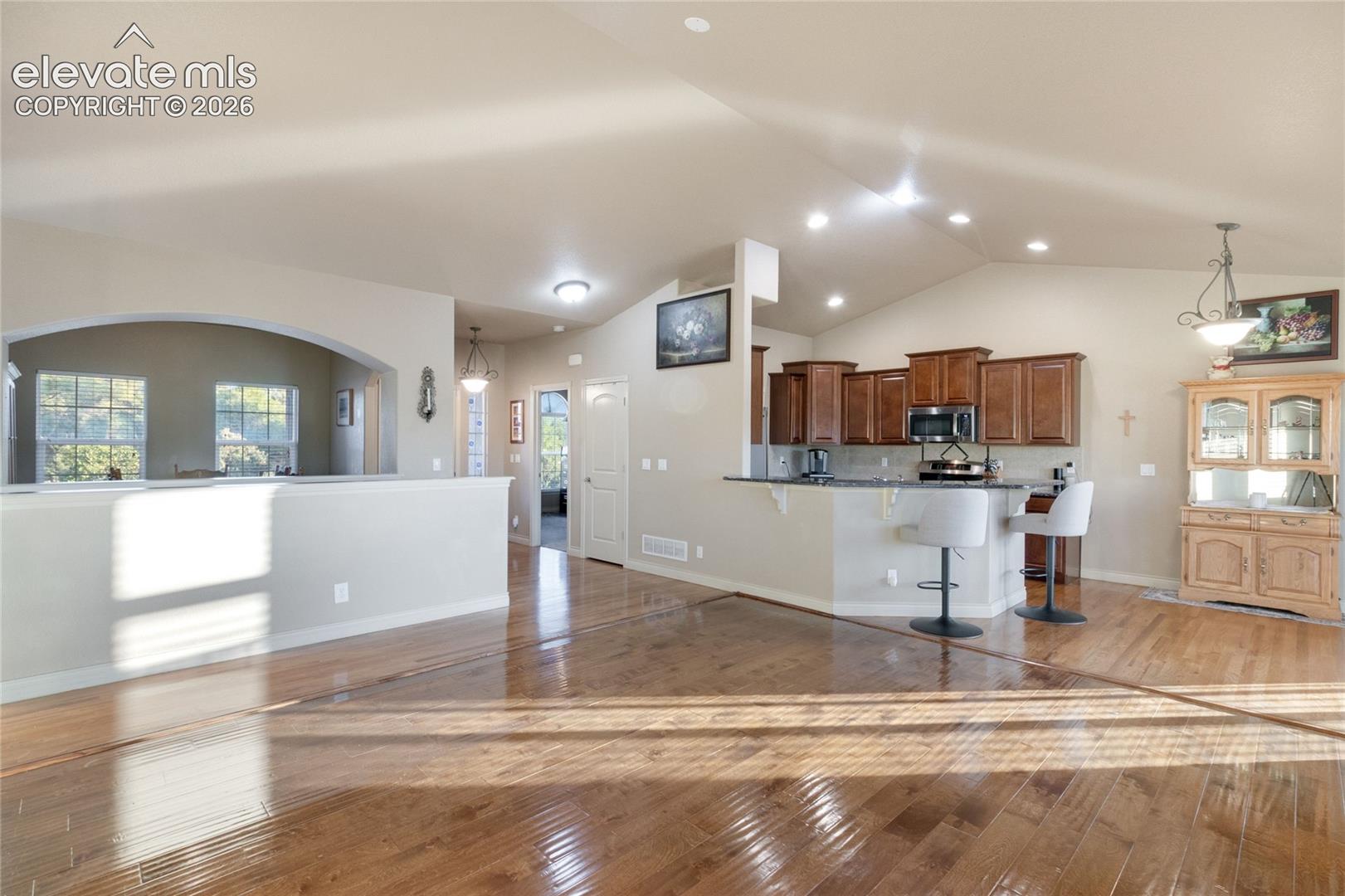 Open-concept interior featuring vaulted ceilings, wood flooring, recessed lighting, and a kitchen peninsula with stone countertops and wood cabinetry