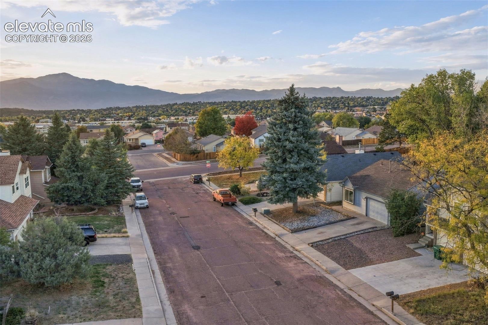Aerial perspective of the residential area featuring mature coniferous and deciduous trees, paved street infrastructure, and mountain topography