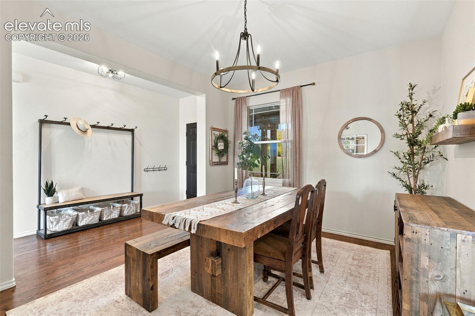 Dining area featuring dark wood-finish flooring, a metal circular chandelier with exposed-bulb styling, and a built-in metal framed bench with coat hooks
