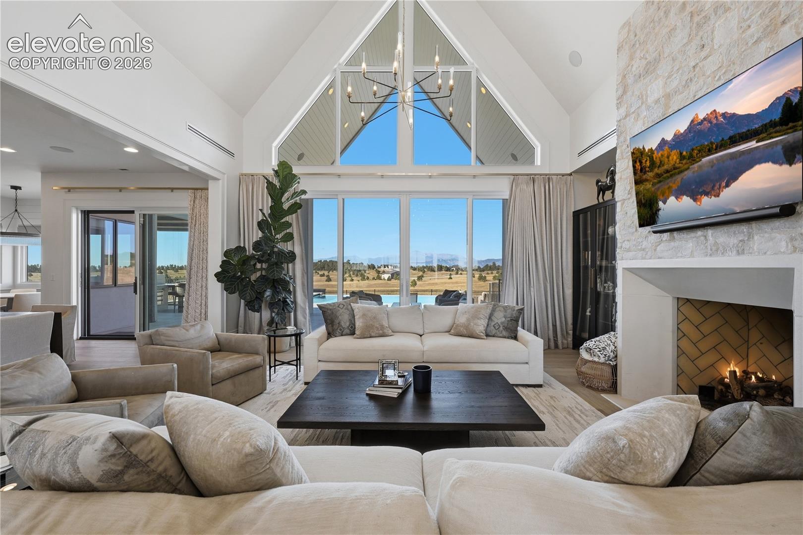 Vaulted ceiling with floor-to-ceiling geometric windows, floor-to-ceiling stone-clad fireplace, and herringbone-patterned firebox