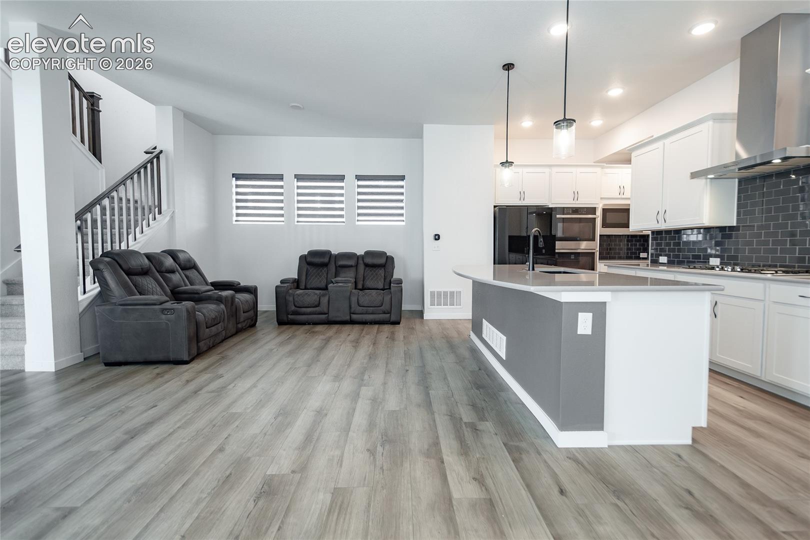 Open concept kitchen featuring a stone-surface island, white cabinetry, dark tile backsplash, stainless steel range hood, and wood-finish flooring