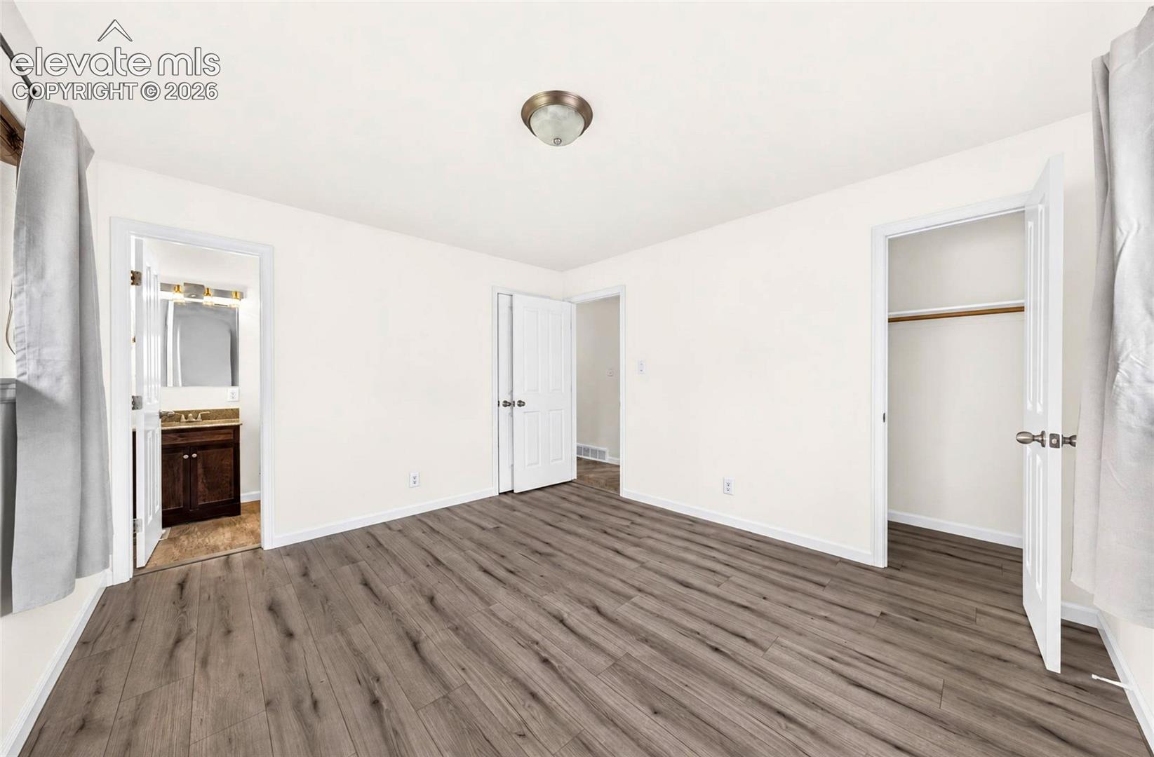 Room featuring wood-finish flooring, white walls, and a closet with a built-in hanging rod