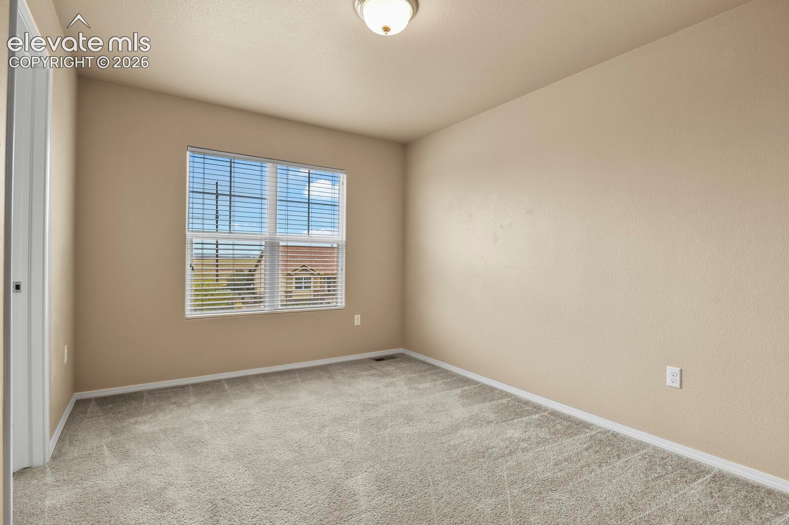 Neutral tone wall paint, light gray carpeting, ceiling-mounted light fixture, and window with horizontal blinds