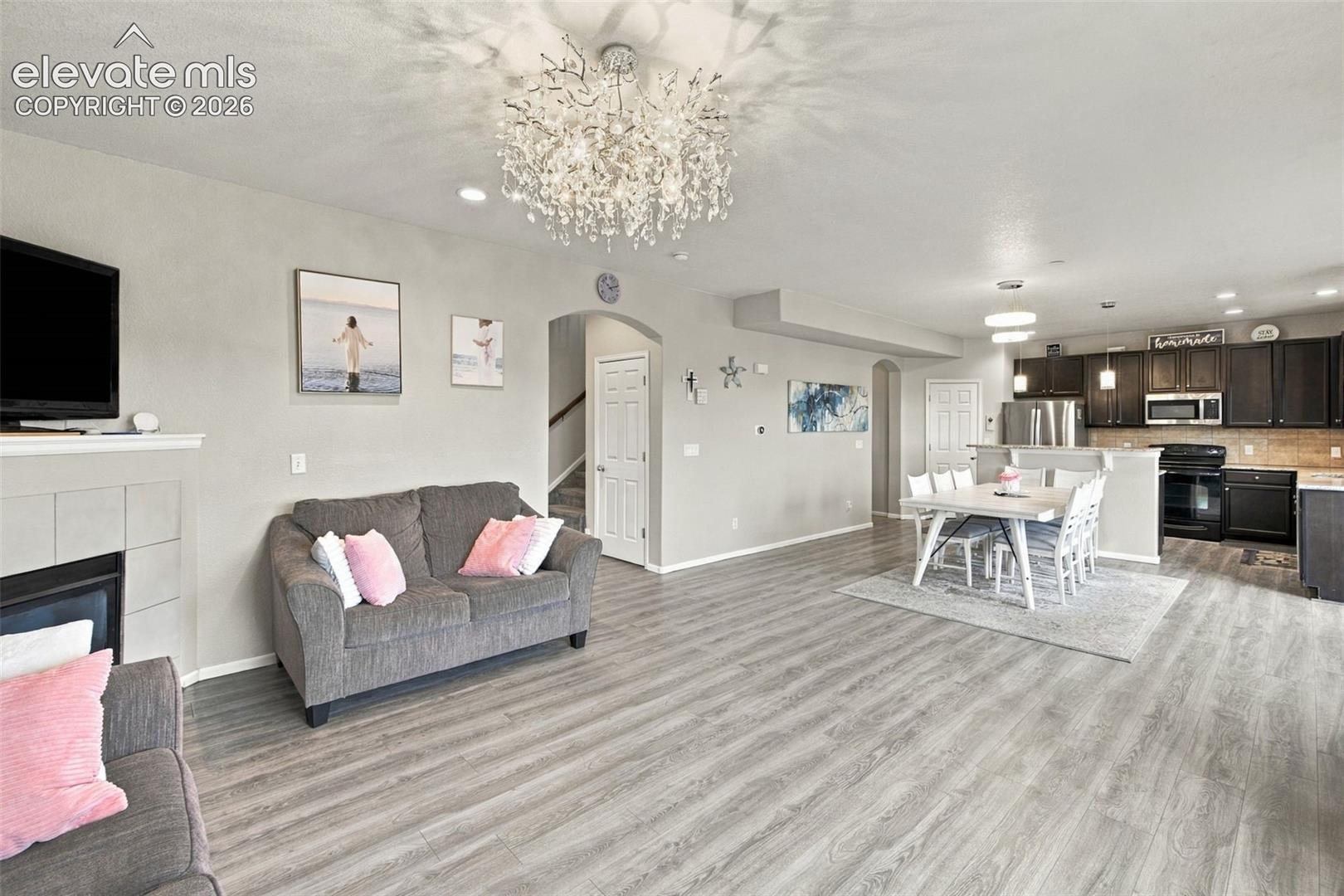 Open-concept interior featuring wood-finish flooring, a decorative crystal chandelier, a neutral fireplace surround, recessed lighting, and kitchen cabinetry