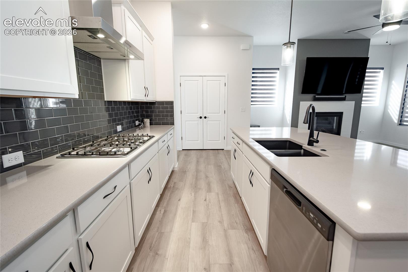 Kitchen featuring a center island, light-toned composite countertops, white cabinetry with matte black hardware, grey subway tile backsplash, and wood-finish flooring