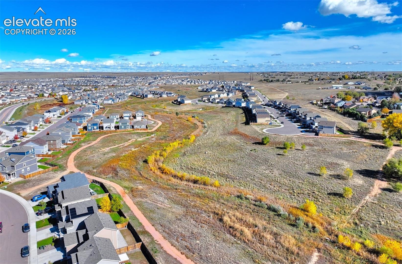 Aerial perspective featuring expansive open space, natural vegetation, meandering earthen paths, and surrounding suburban residential development