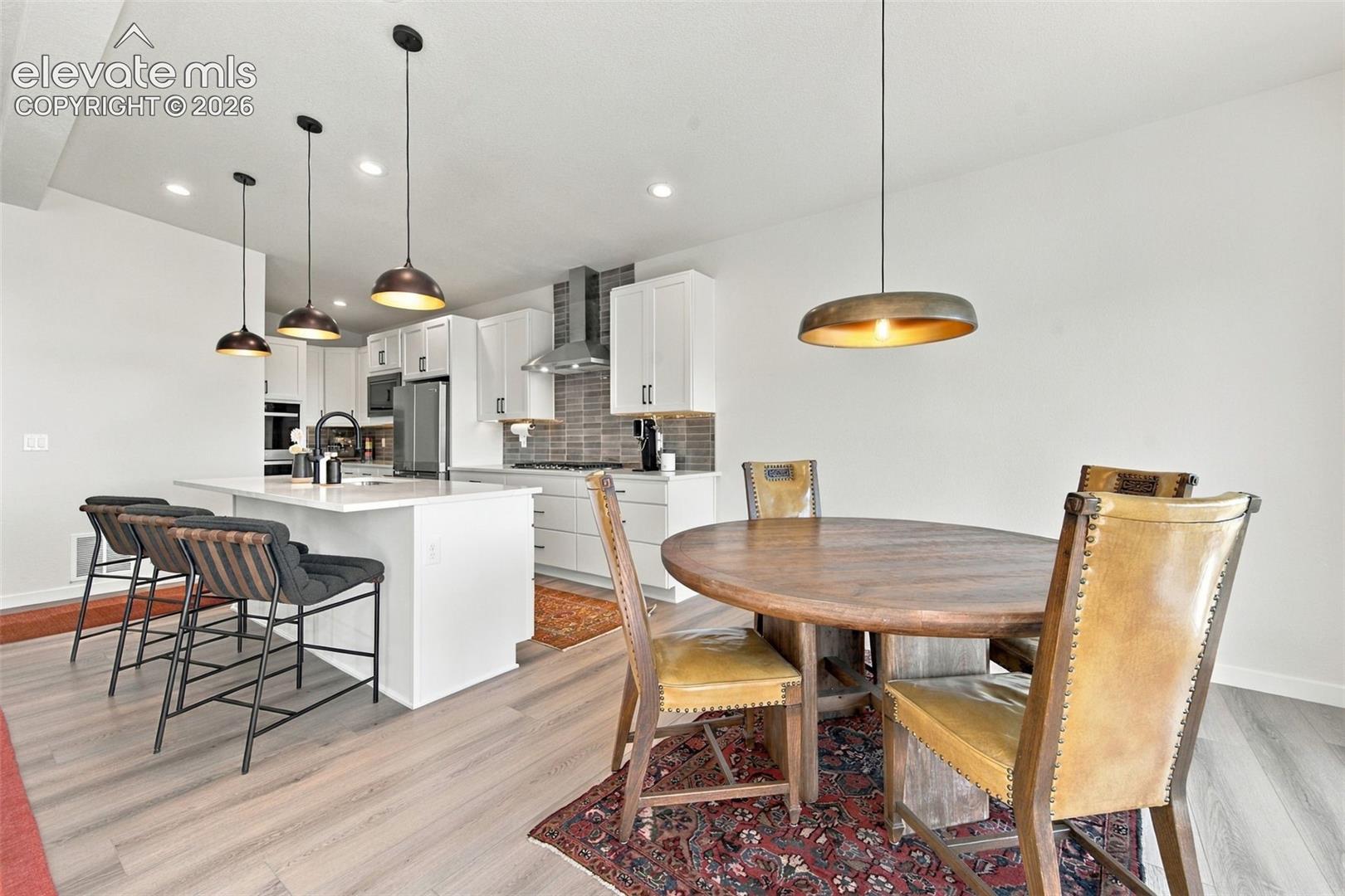 Kitchen featuring white shaker cabinetry, a waterfall-edge island with seating, a subway-tile backsplash, stainless steel appliances, and pendant lighting