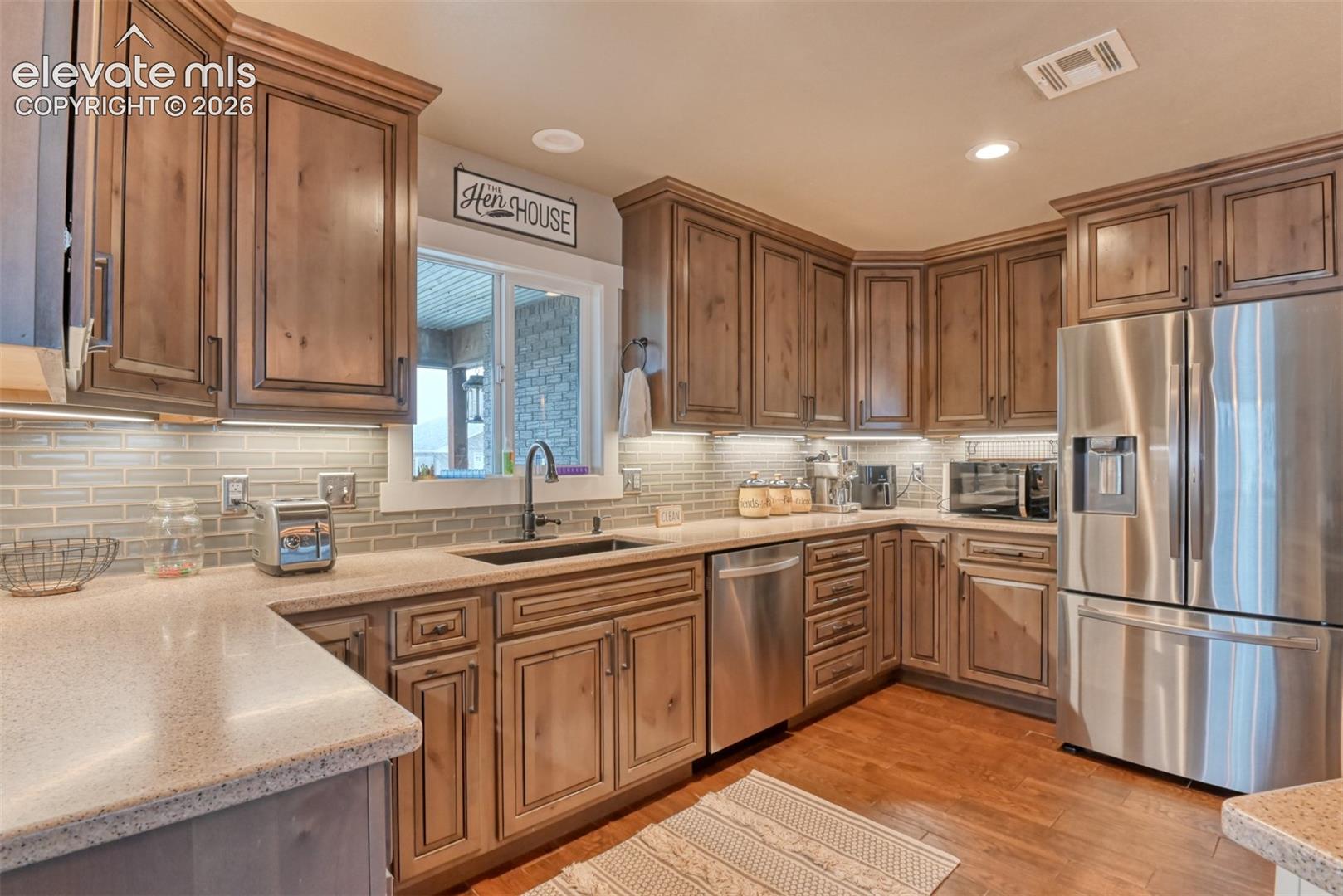Kitchen with stainless steel appliances, light stone countertops, light wood-type flooring, backsplash, and recessed lighting