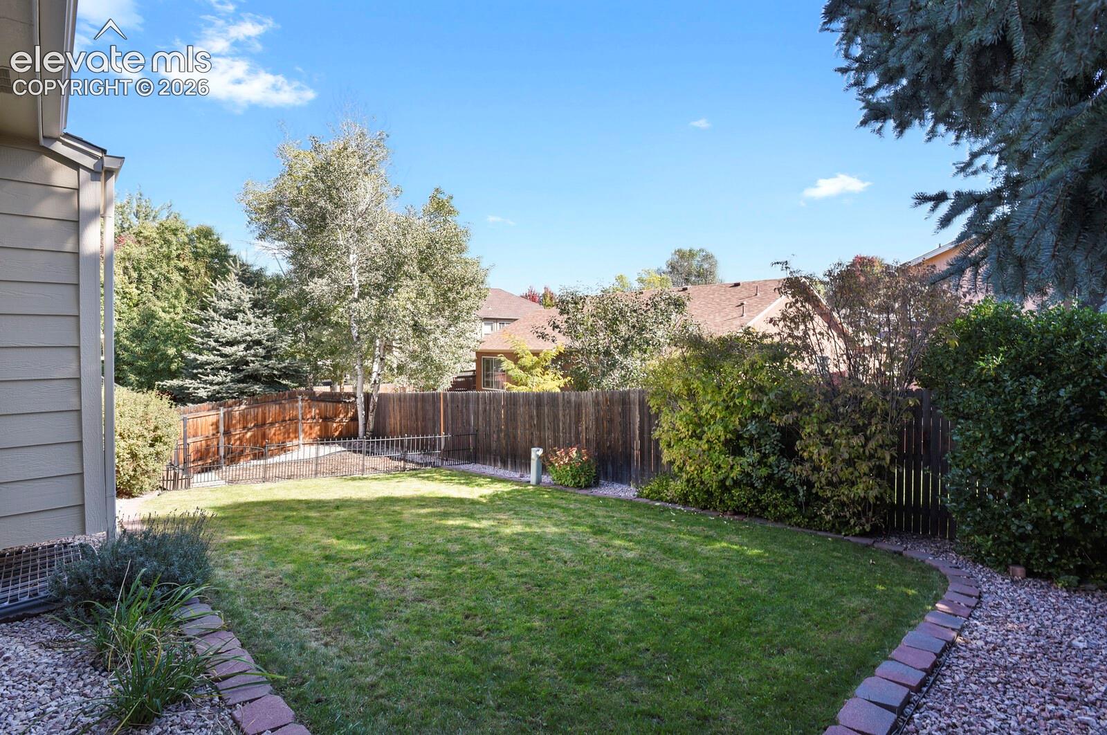 Expansive backyard featuring a manicured lawn, wood fencing, and mature trees