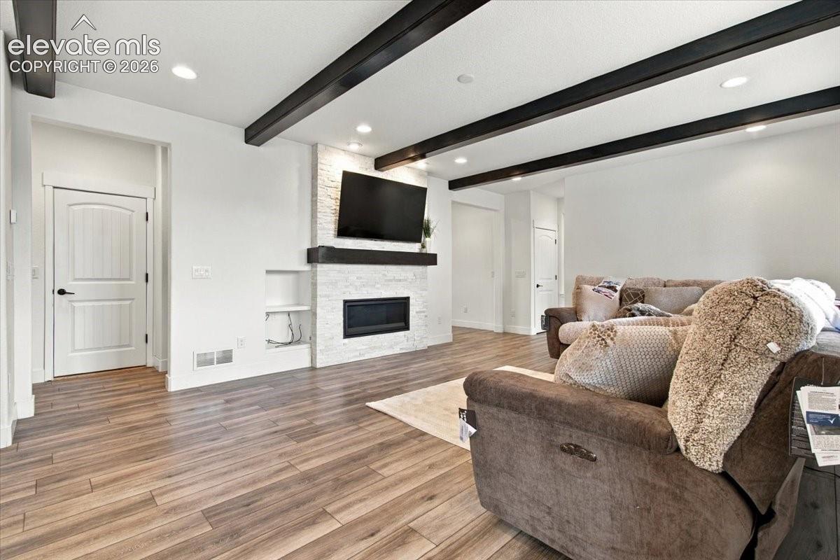 Living area featuring wood-finish flooring, exposed dark ceiling beams, recessed lighting, and a floor-to-ceiling white stone-clad fireplace with a built-in niche