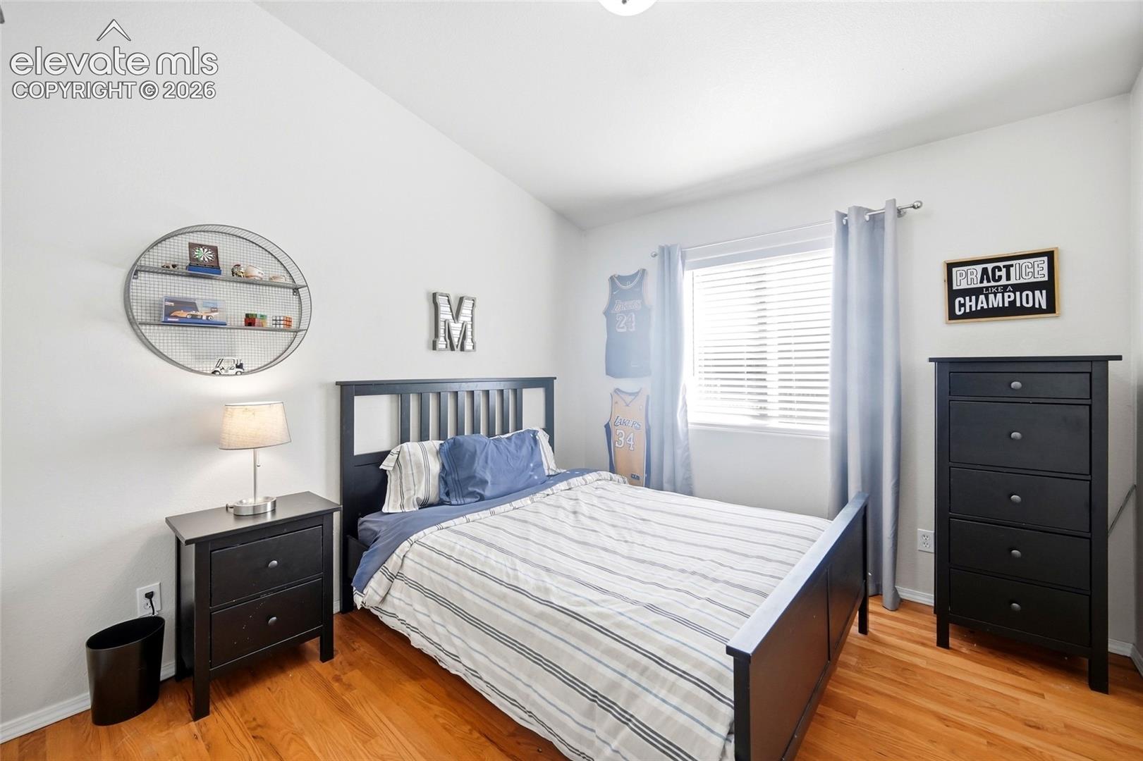 Vaulted ceiling, wood-finish flooring, and a window with blinds