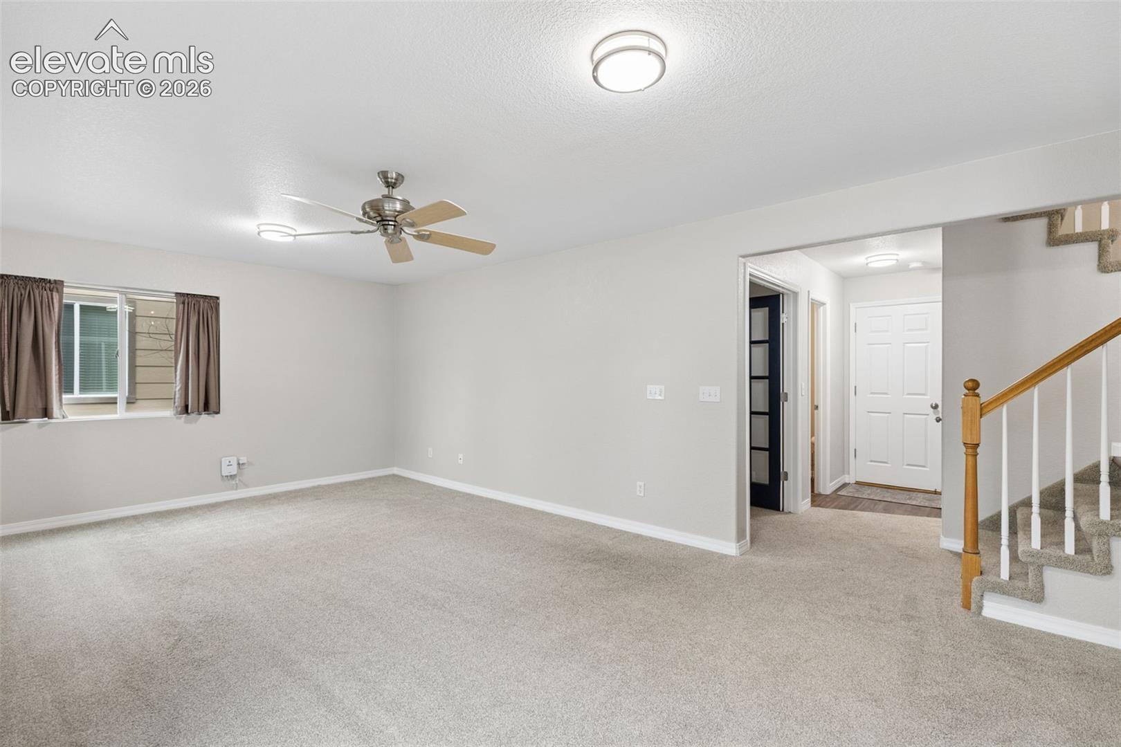 Open-concept interior featuring neutral wall tones, wall-to-wall carpeting, a brushed metal ceiling fan, and a staircase with a wooden handrail and white balusters