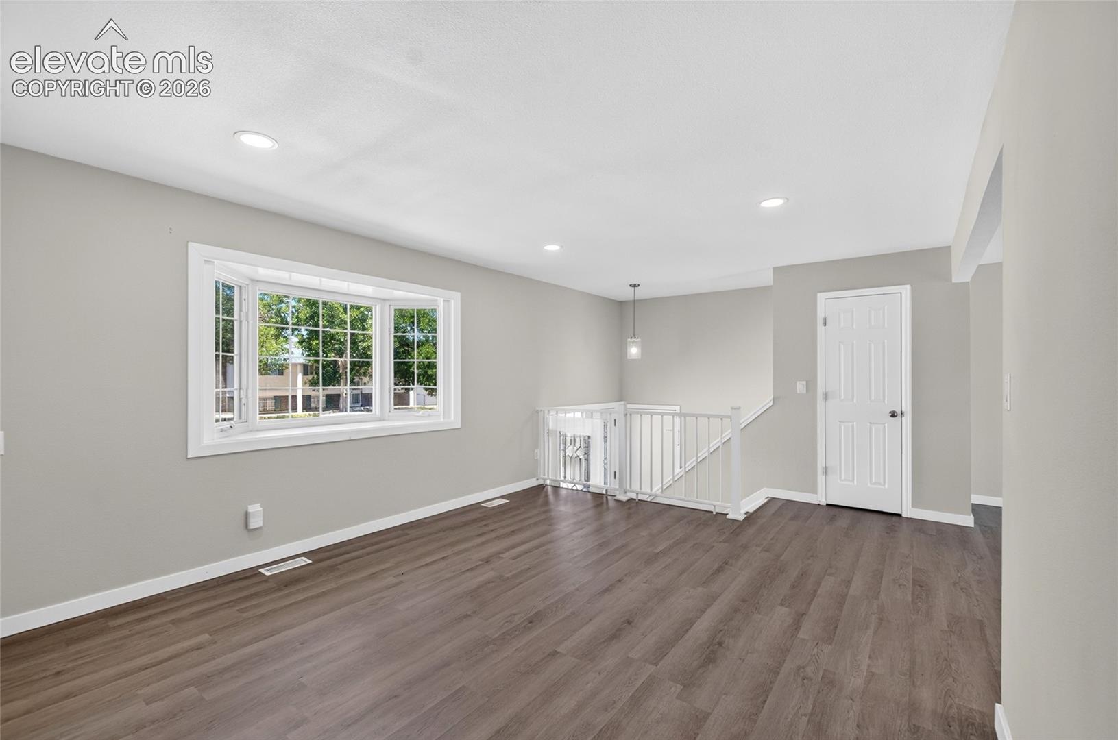Spacious room featuring wood-finish flooring, a large bay window, light gray wall tones, recessed lighting, and a contemporary pendant light fixture