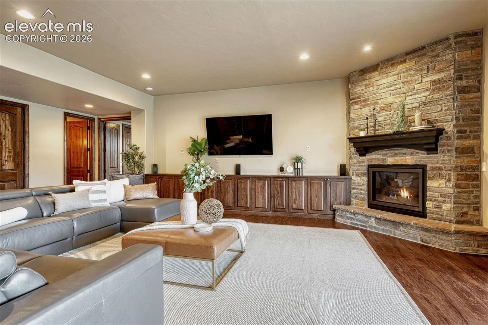 Elegant living room showcasing a gas fireplace with stacked stone surround, built-in wood cabinetry with shelving, hardwood flooring, and recessed ceiling lighting