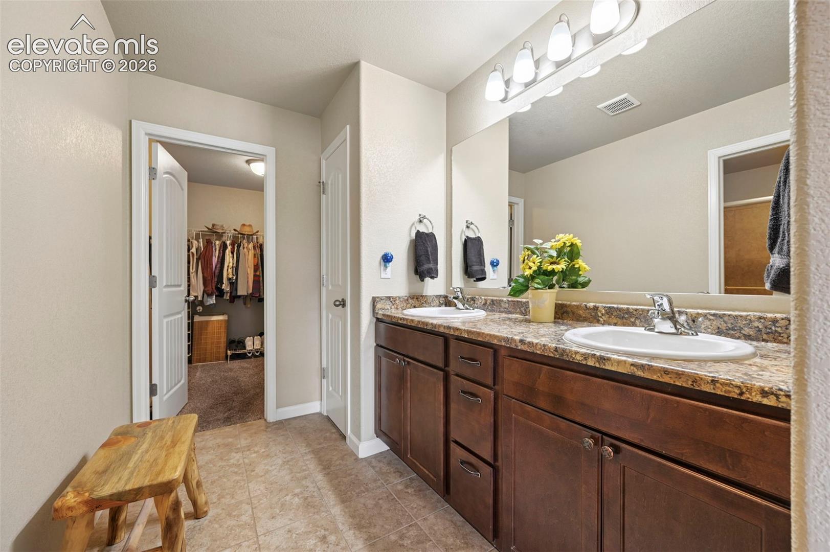 Primary Bathroom featuring a dual vanity with a patterned countertop and wood-finish cabinetry