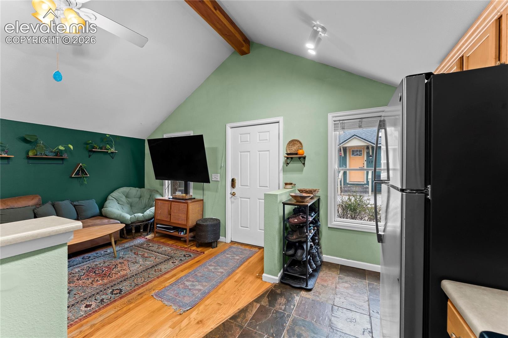 Vaulted ceiling featuring an exposed wood beam, natural wood-finish flooring, and stone-tile flooring