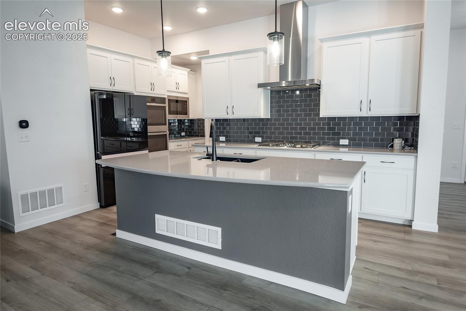 Kitchen featuring white shaker-style cabinetry, a contrasting gray tile backsplash, stone-finish countertops, stainless steel appliances, and wood-finish flooring
