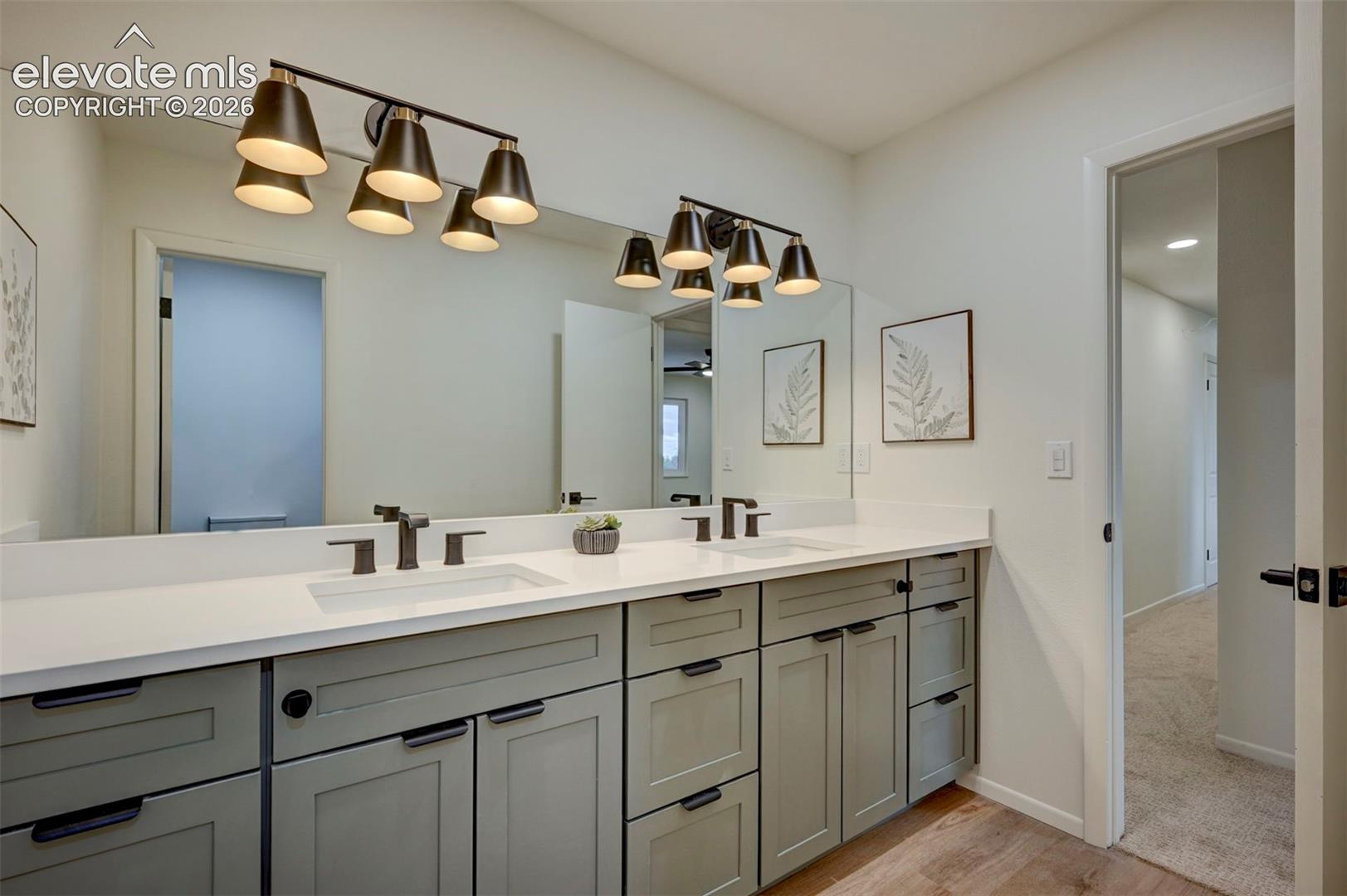Dual-sink vanity featuring grey cabinetry, solid-surface white countertops, undermount sinks, and matte black fixtures, illuminated by two multi-light vanity sconces with large wall-to-wall mirror
