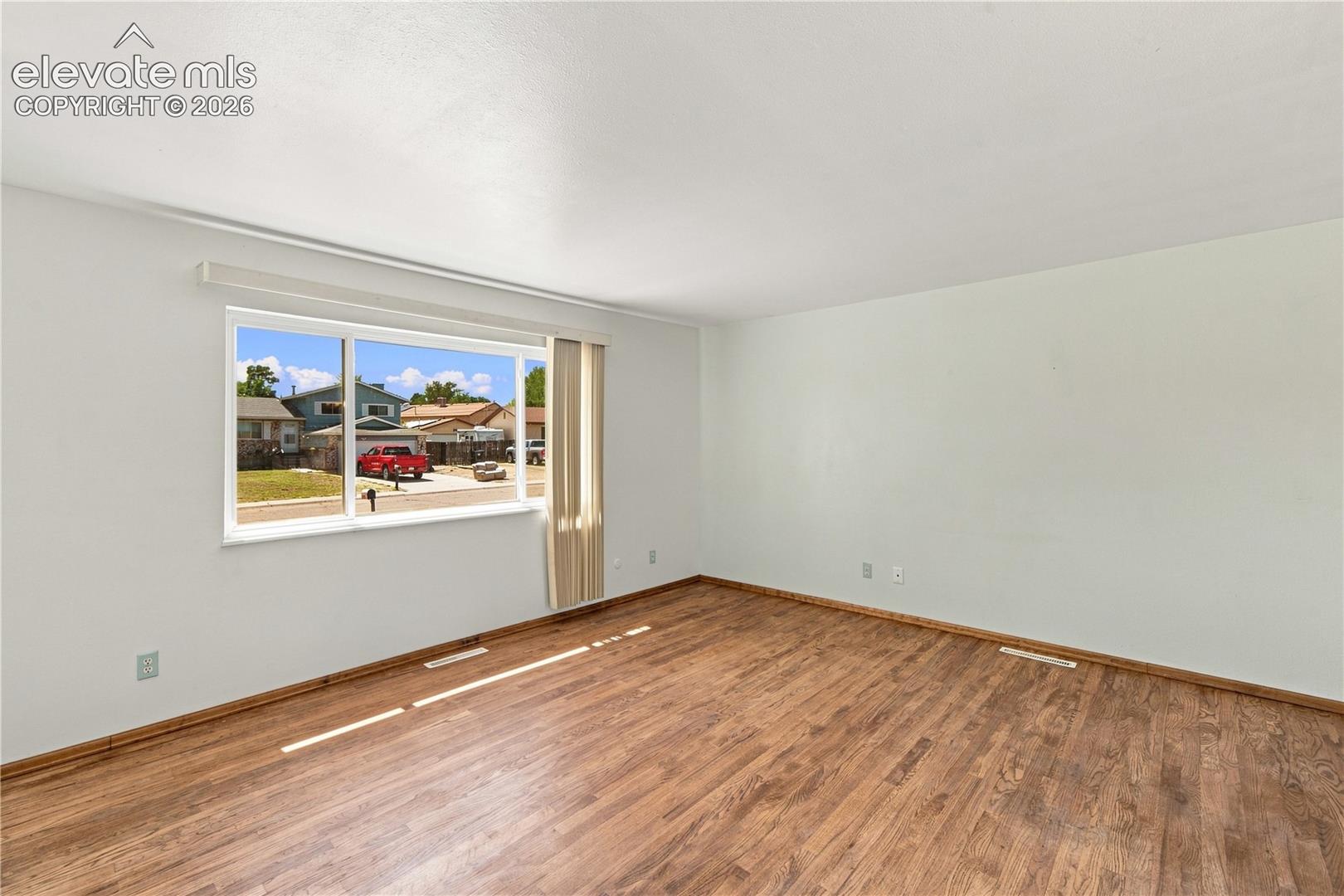 Spacious room featuring wood-finish flooring, white walls, and a large window