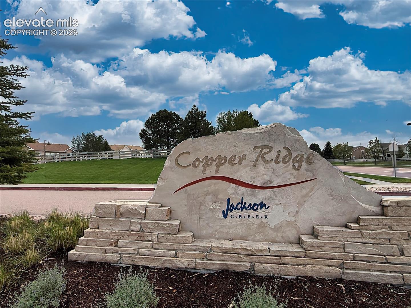 Welcoming entrance monument for the Copper Ridge at Jackson Creek community, surrounded by mature landscaping, open green space, and scenic Colorado skies.