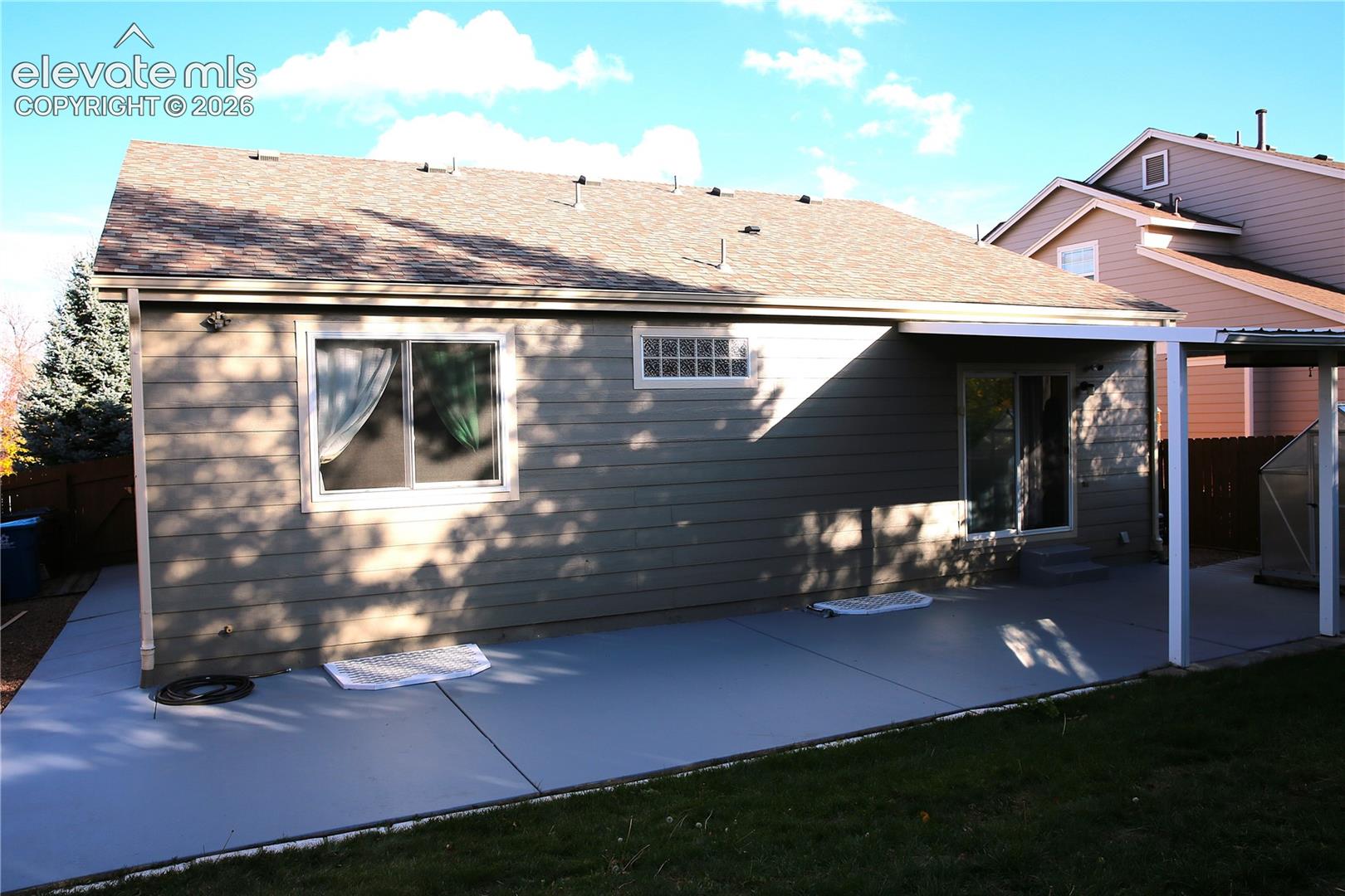 Exterior rear elevation featuring horizontal siding, a covered concrete patio, sliding glass door, and a multi-pane accent window