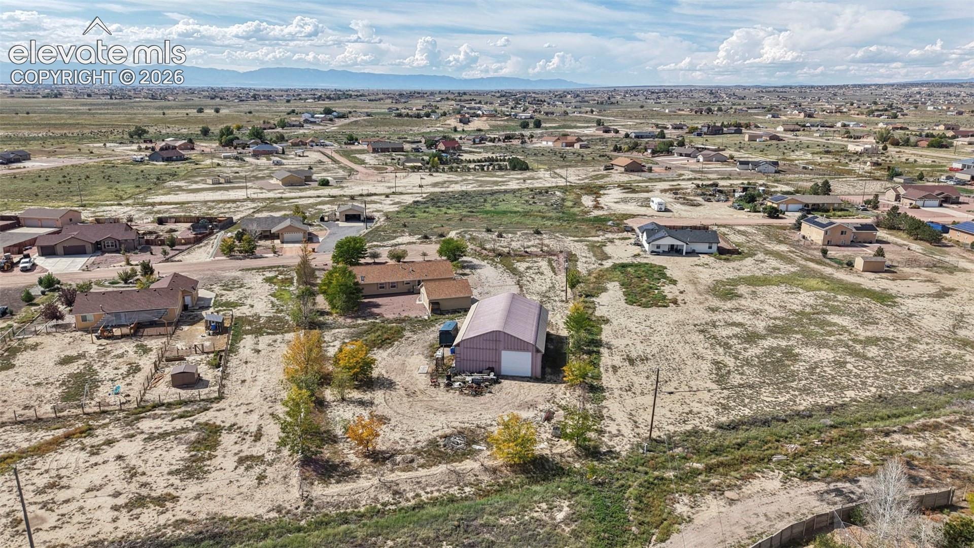 Expansive lot featuring a detached metal-sided workshop, mature trees, and mountain horizon