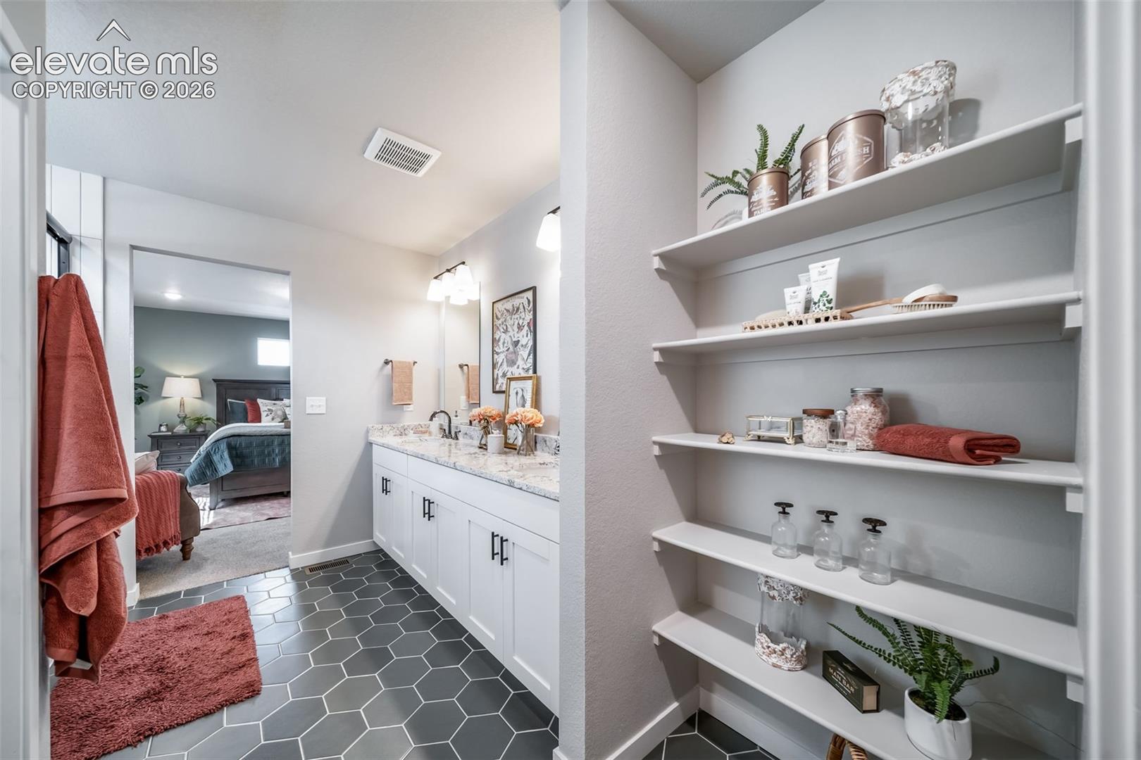 Bathroom featuring hexagonal floor tiling, a double vanity with white cabinetry and a light-toned countertop, and a built-in shelving unit
*Photos of a model home*