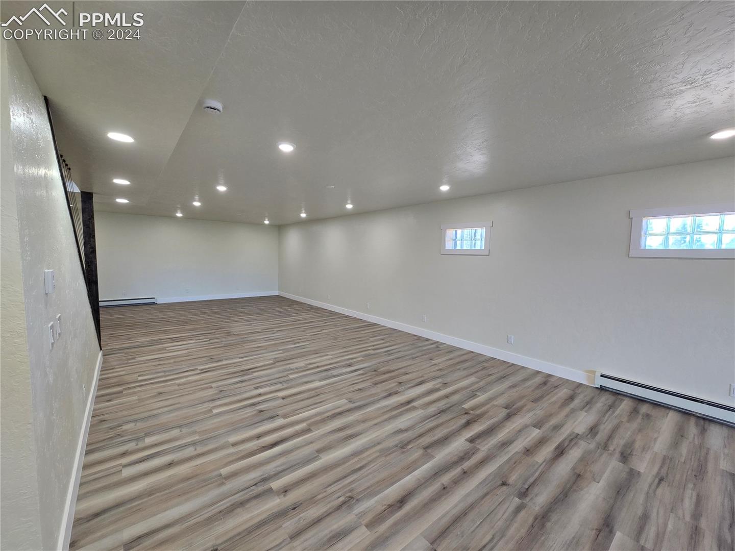 Basement with a textured ceiling, light hardwood / wood-style flooring, and baseboard heating