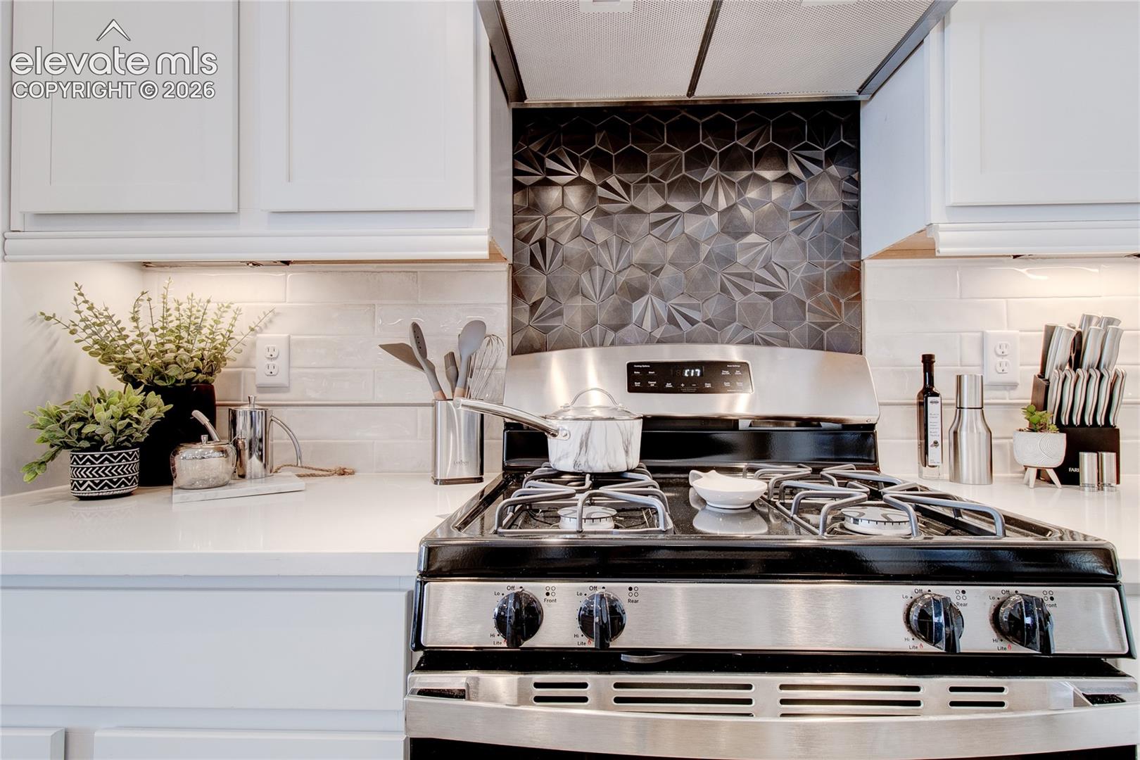 Kitchen featuring white shaker-style cabinetry, a solid-surface countertop, stainless steel gas range, geometric-patterned tile backsplash, and subway-tile wall cladding