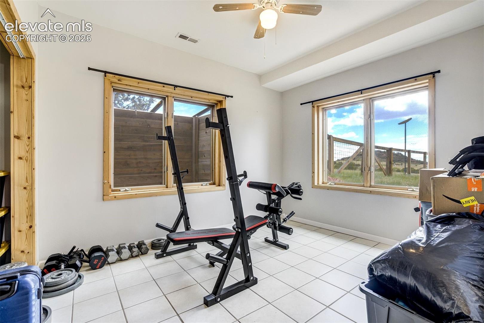 Versatile room featuring two windows with natural wood trim, white tile flooring, a built-in wood-finish shelving unit, a ceiling fan, and recessed lighting