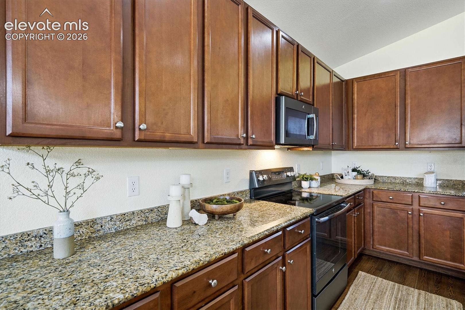 Kitchen featuring wood-finish cabinetry, speckled countertops, stainless steel appliances, and under-cabinet lighting