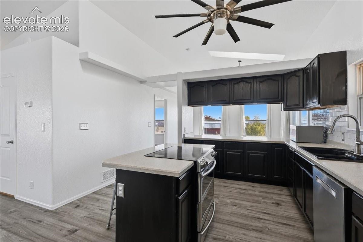 Kitchen featuring dark cabinetry, solid-surface countertops, wood-finish flooring, vaulted ceilings, and a ceiling fan with integrated lighting