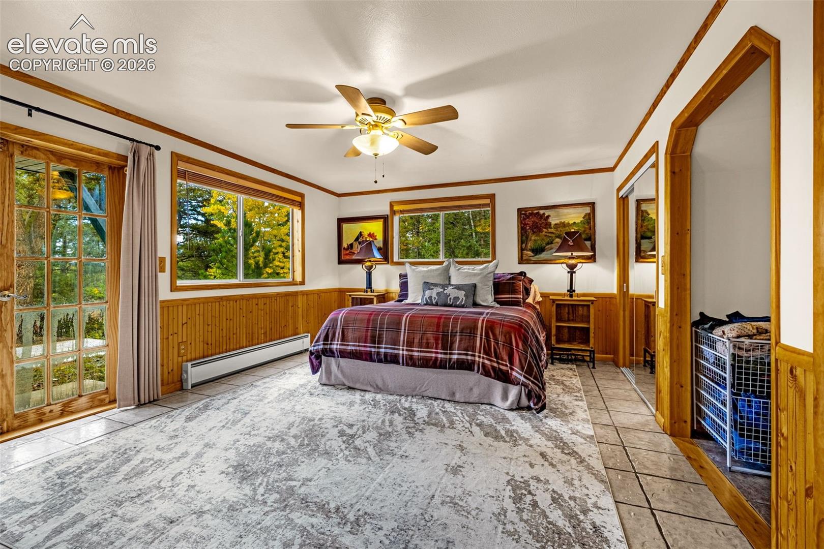 Room featuring wood wainscoting, a multi-pane glass door, tile flooring, and a ceiling fan with integrated lighting