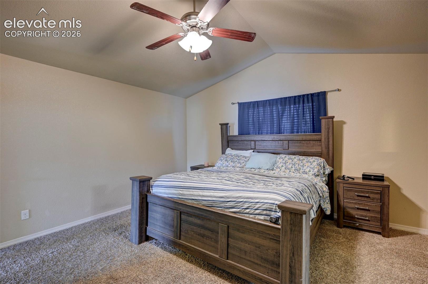 Vaulted ceiling with a wood-finish ceiling fan, neutral wall tones, and carpeted flooring