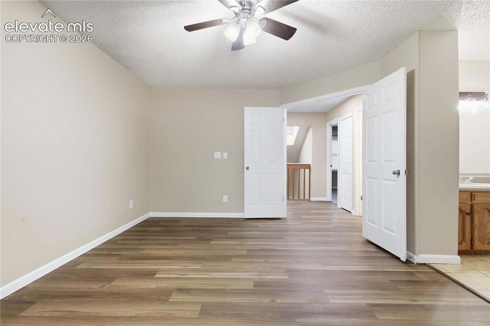 Expansive room featuring wood-finish flooring, light-toned walls, and a ceiling fan with integrated lighting