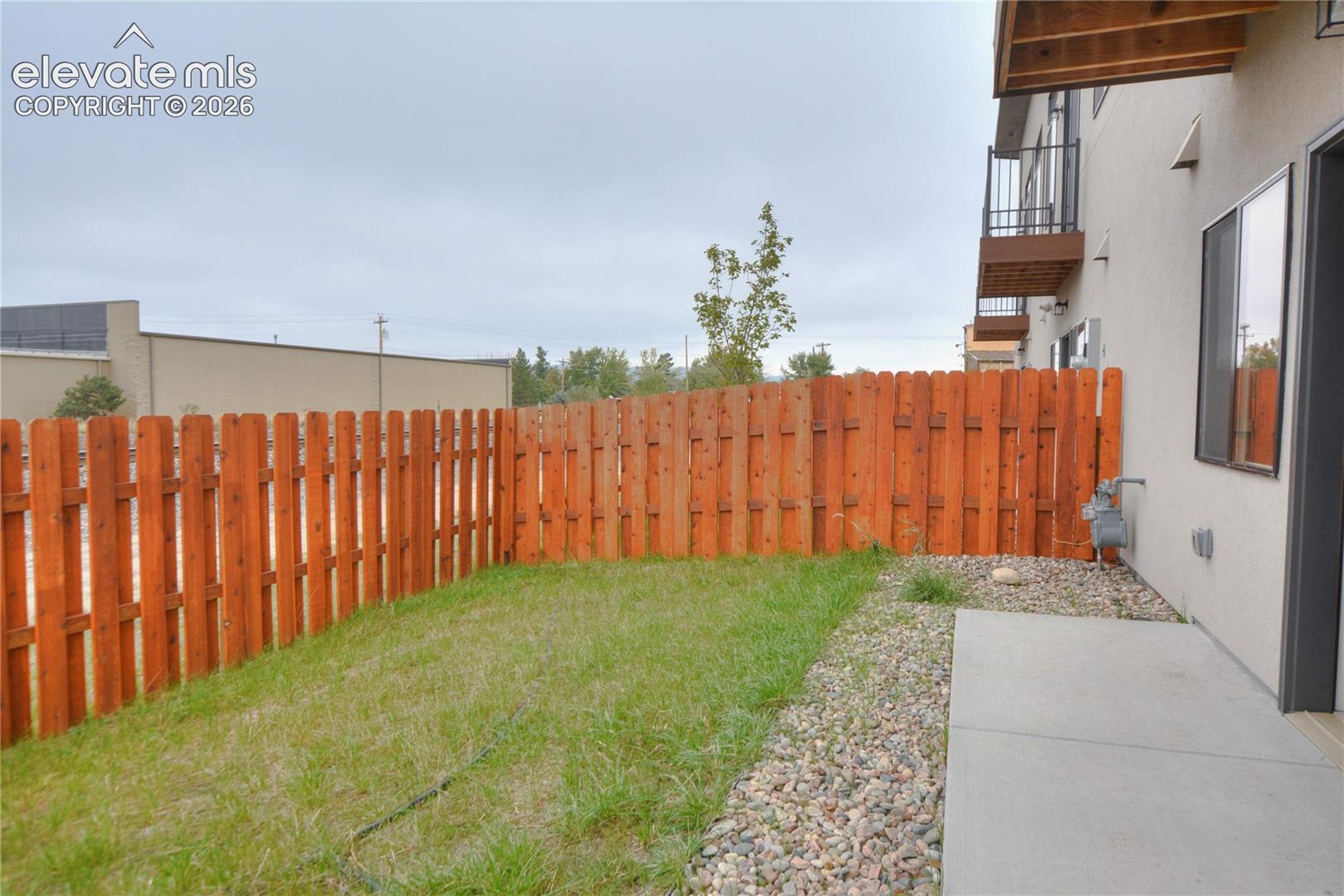 Private outdoor space featuring a wood fence, a patch of grass, and a concrete patio with an adjacent gravel bed