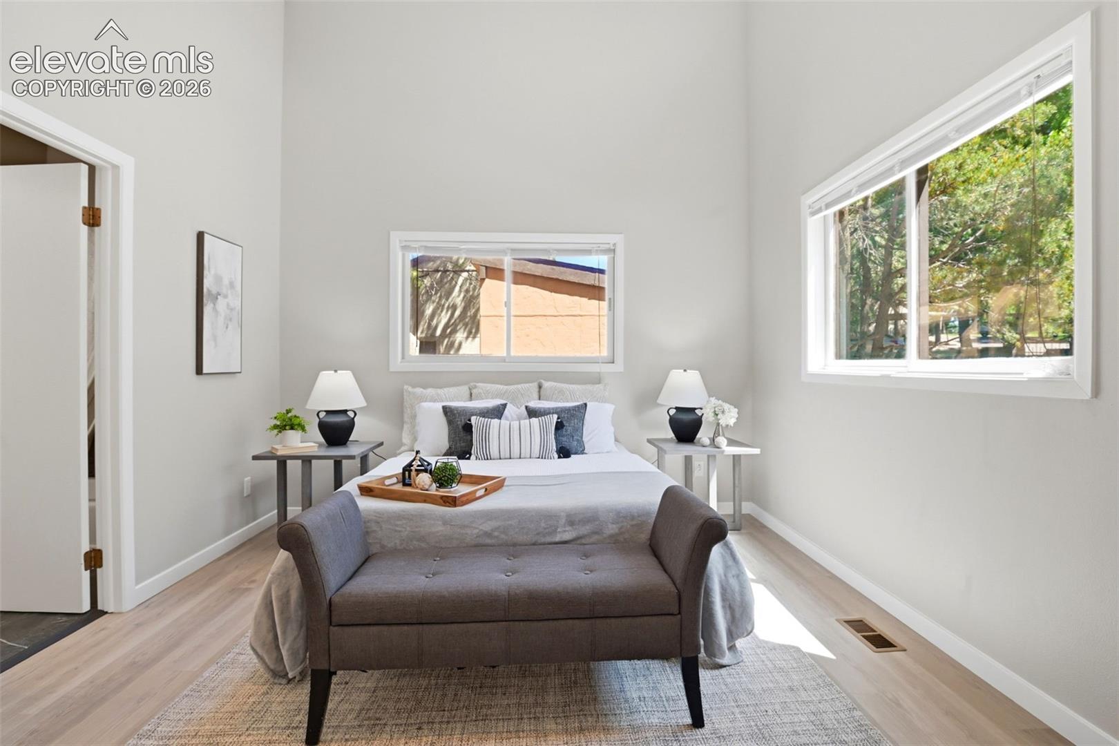 Light-filled bedroom featuring vaulted ceilings, light wood-finish flooring, and multiple windows