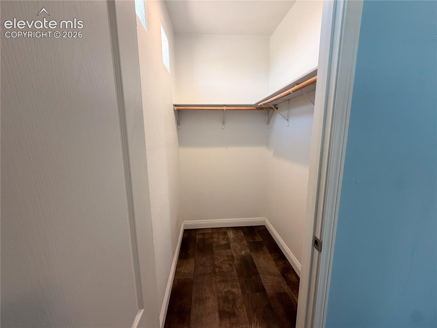 Walk-in closet featuring wood-finish flooring, built-in shelving, and a mounted hanging rod