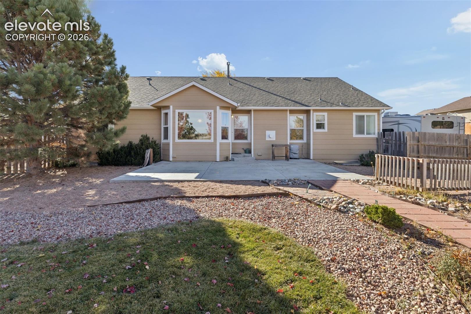 Rear exterior featuring horizontal lap siding, concrete patio, bay window, and xeriscaped grounds with paver walkway