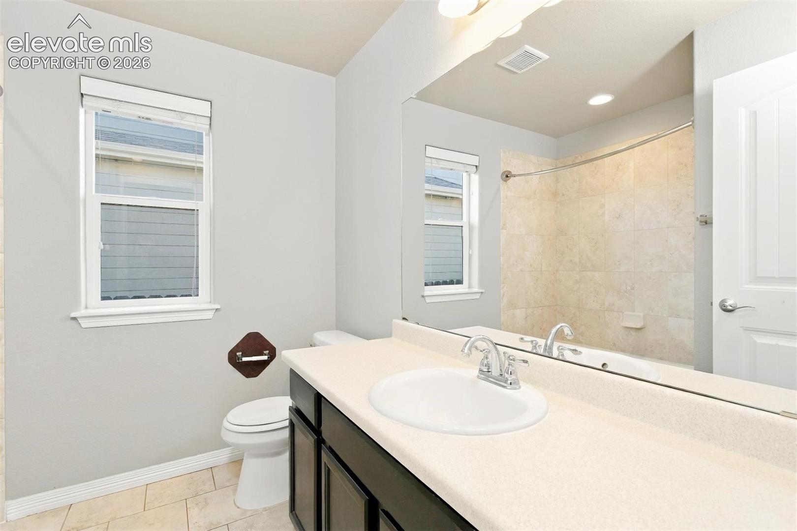 Vanity with a solid-surface countertop and integrated sink, large wall-mounted mirror, ceramic tile shower surround, and tile flooring