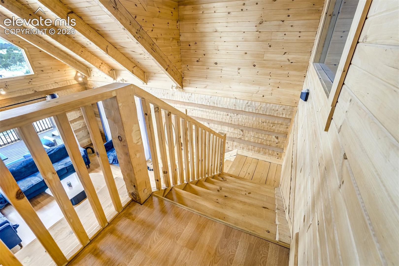 Wood-finish stairs with a coordinating wood railing, wood-paneled walls, and exposed wood beams